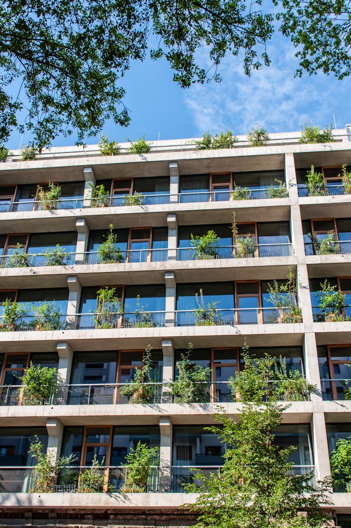 A contemporary building facade featuring lush greenery and glass windows under a clear sky.